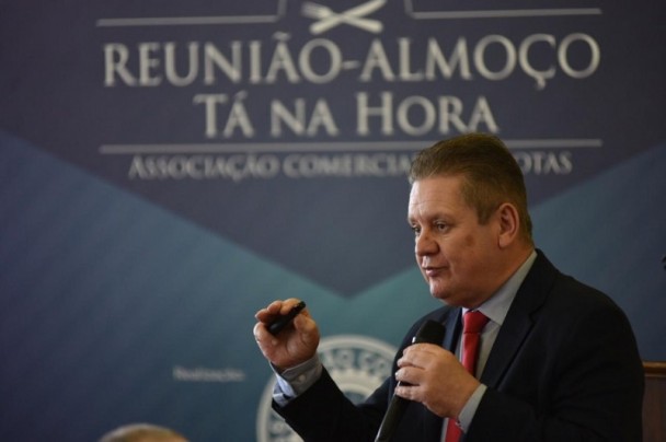 A imagem mostra o bice-governador Ranolfo Vieira Júnior em discurso com um banner da reunião-almoço Tá na Hora da Associação Comercial de Pelotas ao fundo.