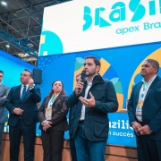 V&aacute;rias pessoas est&atilde;o reunidas em um palco, com uma delas mais ao centro falando ao microfone.